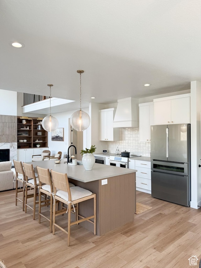 kitchen featuring backsplash, light wood-style flooring, freestanding refrigerator, custom exhaust hood, and white cabinetry