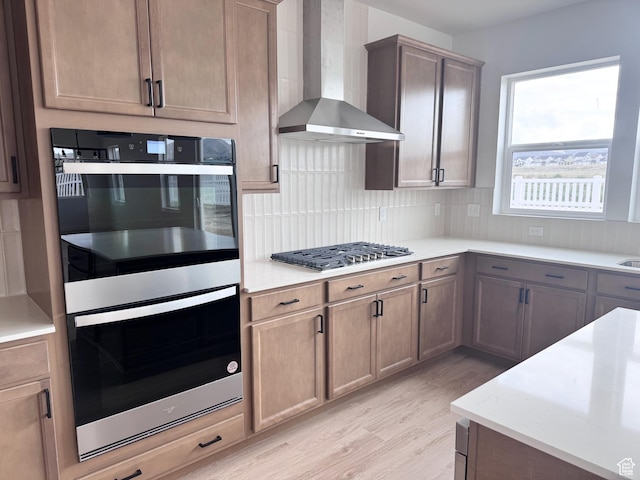 189 N Woodrun Way Unit 131, Saratoga Springs, UT 84045 - kitchen featuring wall chimney exhaust hood, multiple ovens, light wood-style flooring, decorative backsplash, and light countertops