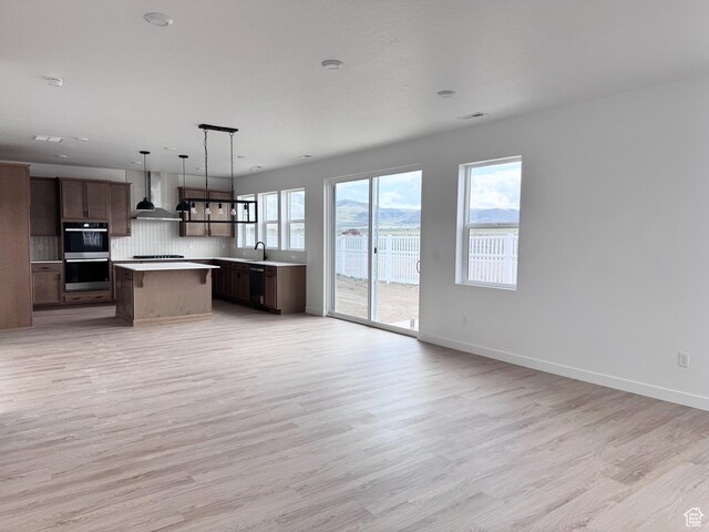 189 N Woodrun Way Unit 131, Saratoga Springs, UT 84045 - kitchen featuring wall chimney range hood, open floor plan, light countertops, light wood-style flooring, and a center island