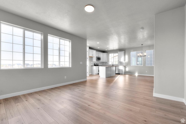 6644 W Spring Snow Ln, Herriman, UT 84096 - unfurnished living room with a chandelier, a textured ceiling, light wood finished floors, and recessed lighting