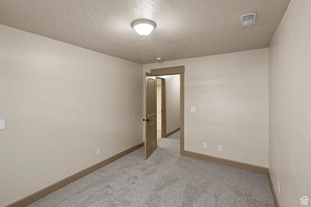 spare room with visible vents, a textured ceiling, baseboards, and light colored carpet