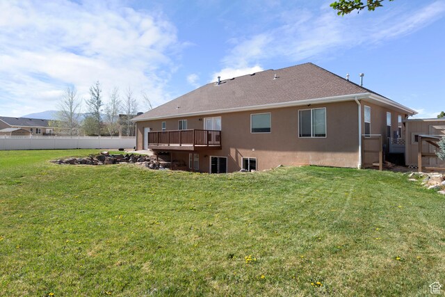 back of property featuring a fire pit, fence, a deck, stucco siding, and a yard