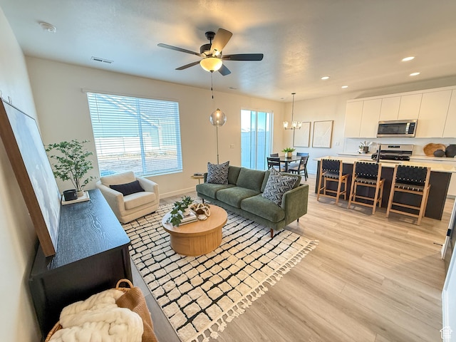 living room with visible vents, a healthy amount of sunlight, light wood finished floors, and ceiling fan with notable chandelier