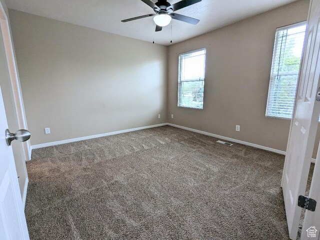 carpeted empty room featuring visible vents, a ceiling fan, and baseboards