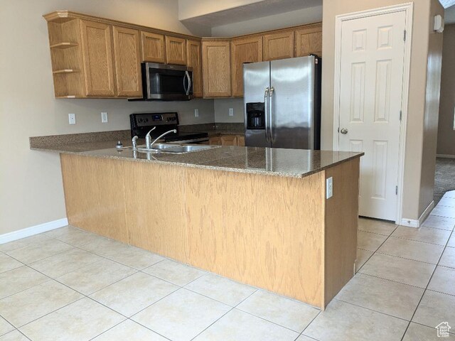 kitchen with appliances with stainless steel finishes, brown cabinetry, dark stone countertops, a peninsula, and light tile patterned floors
