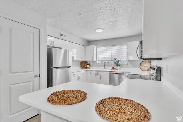 1140 W 950 N Unit E202, Orem, UT 84057 - kitchen featuring a peninsula, light countertops, a textured ceiling, white cabinets, and appliances with stainless steel finishes