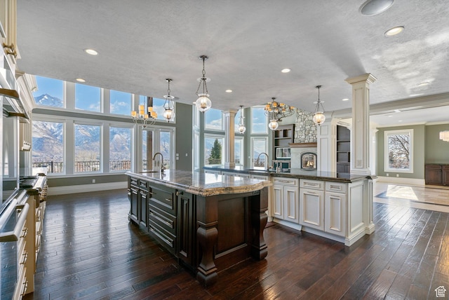 kitchen with decorative columns, dark wood finished floors, a spacious island, baseboards, and an inviting chandelier