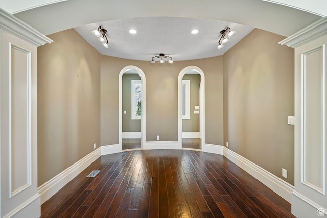 unfurnished room featuring visible vents, arched walkways, track lighting, baseboards, and wood-type flooring