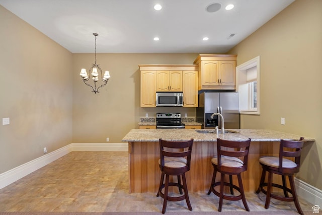 kitchen with light brown cabinetry, a breakfast bar, baseboards, a sink, and appliances with stainless steel finishes