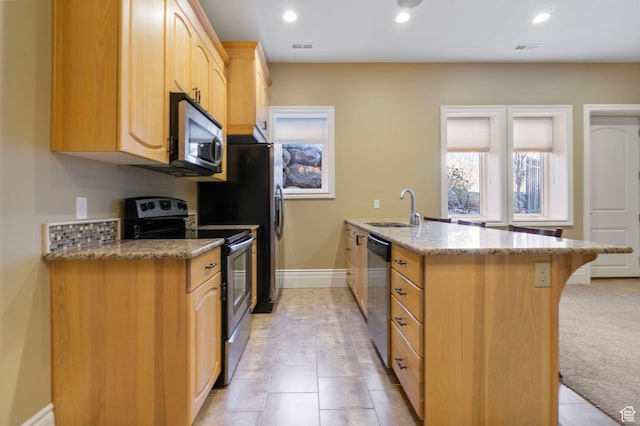 kitchen with a kitchen bar, appliances with stainless steel finishes, light brown cabinetry, a sink, and light stone counters