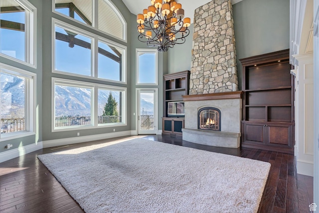 living area with a towering ceiling, baseboards, dark wood-style floors, a large fireplace, and a notable chandelier