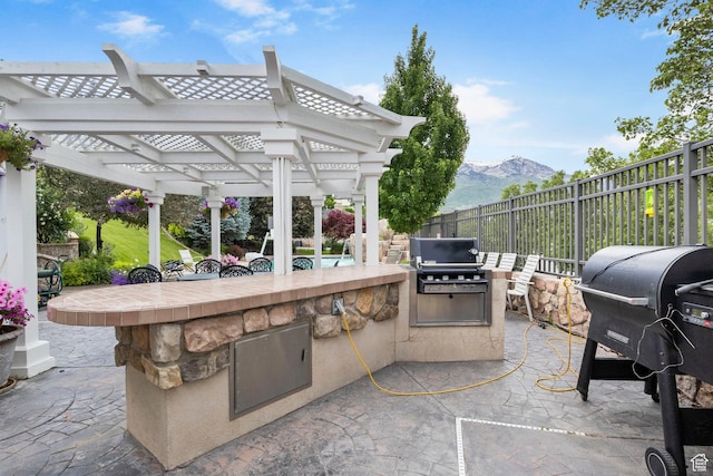 view of patio / terrace featuring grilling area, fence, a mountain view, an outdoor kitchen, and a pergola