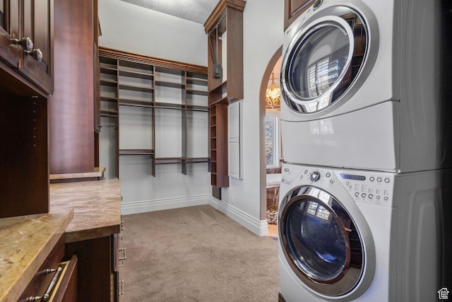 laundry area featuring light colored carpet, stacked washer and dryer, cabinet space, and baseboards