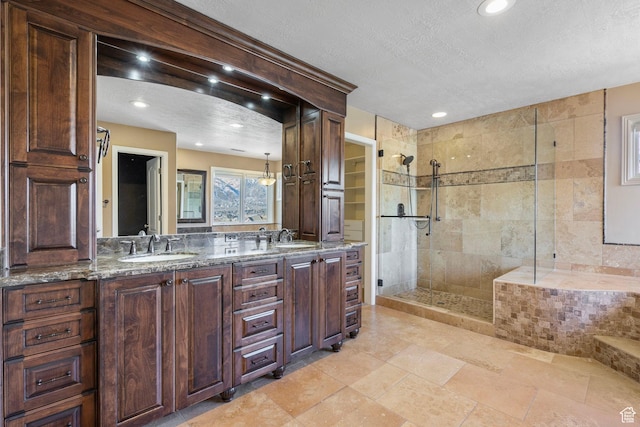 bathroom featuring double vanity, a textured ceiling, a tile shower, and a sink