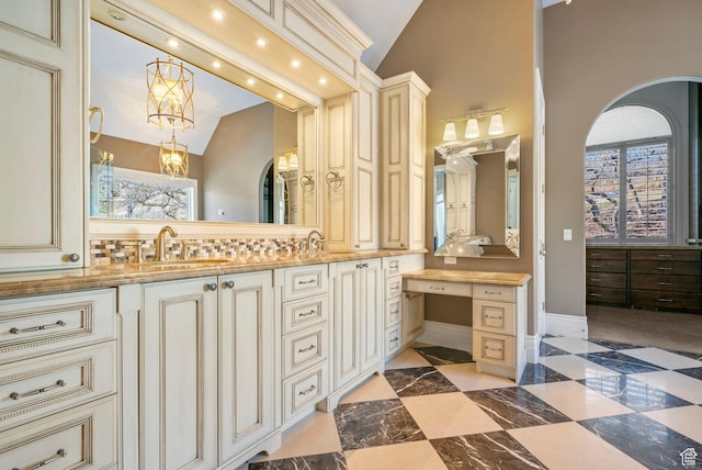 bathroom with a sink, baseboards, double vanity, and lofted ceiling