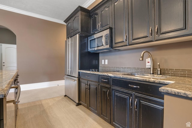 kitchen featuring appliances with stainless steel finishes, arched walkways, a sink, stone countertops, and ornamental molding