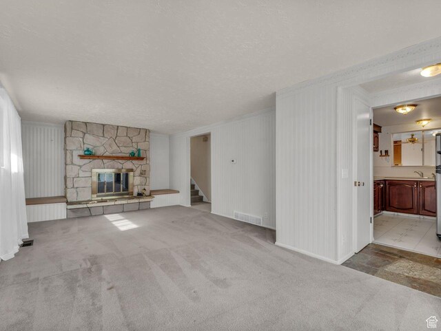 5362 W Elaine Ave, West Valley City, UT 84120 - unfurnished living room featuring a stone fireplace, a textured ceiling, visible vents, carpet, and stairs