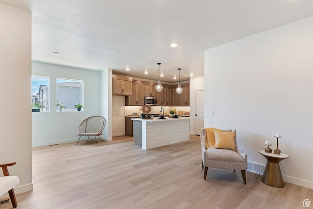 4888 W Coulter Unit 703, Highland, UT 84003 - kitchen with stainless steel microwave, light countertops, light wood-style flooring, a kitchen island with sink, and pendant lighting