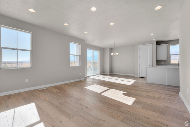 unfurnished living room featuring visible vents, baseboards, a chandelier, light wood-style floors, and recessed lighting