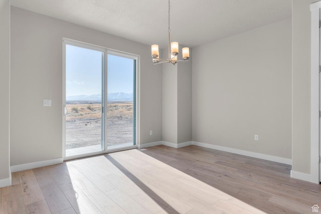 unfurnished room featuring an inviting chandelier, baseboards, a mountain view, and light wood-type flooring