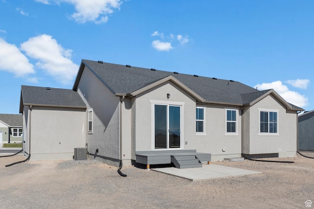back of property with central AC unit, a shingled roof, and stucco siding