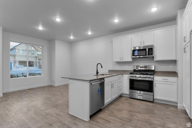kitchen with appliances with stainless steel finishes, light wood-type flooring, a sink, a peninsula, and white cabinetry