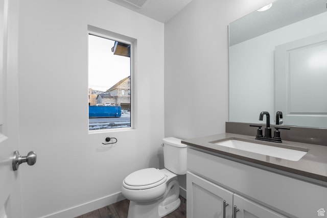 half bath with toilet, baseboards, wood finished floors, and vanity