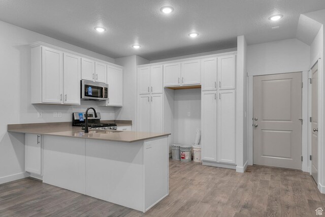 kitchen with appliances with stainless steel finishes, white cabinets, a peninsula, recessed lighting, and light wood-style flooring