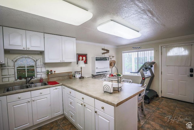kitchen featuring crown molding, stone tile floors, a peninsula, white cabinets, and a sink