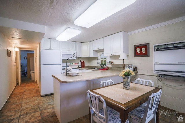 kitchen featuring a textured ceiling, a sink, a peninsula, white appliances, and white cabinetry