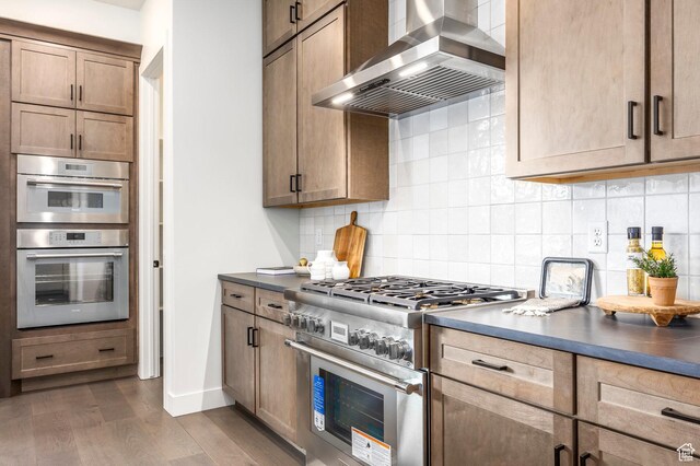 359 N Abajo Peak Loop E Unit A3, Heber City, UT 84032 - kitchen featuring dark countertops, wall chimney range hood, tasteful backsplash, dark wood finished floors, and appliances with stainless steel finishes