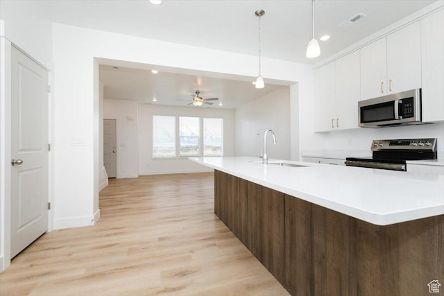 kitchen featuring appliances with stainless steel finishes, a sink, light countertops, light wood-style flooring, and white cabinetry