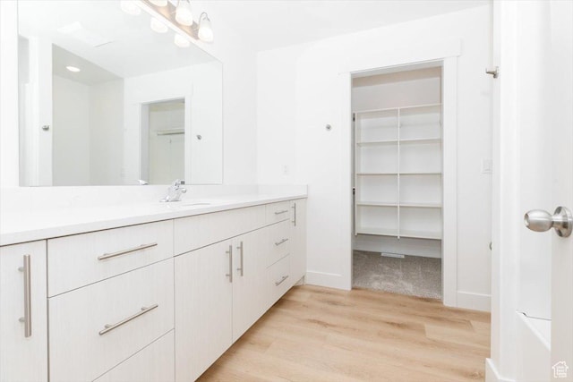 bathroom featuring vanity, baseboards, wood finished floors, and a spacious closet