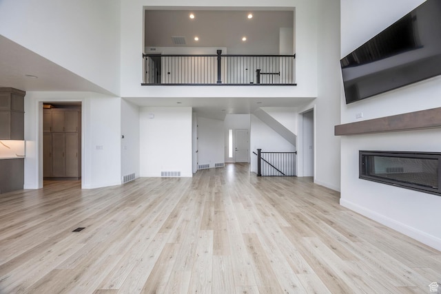5081 W Sequoia Cir, Highland, UT 84003 - unfurnished living room with light wood-style floors, a high ceiling, a glass covered fireplace, and visible vents