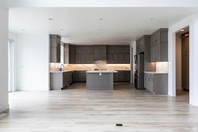 5081 W Sequoia Cir, Highland, UT 84003 - kitchen featuring light countertops, light wood-style flooring, freestanding refrigerator, decorative backsplash, and a kitchen island