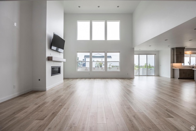 5081 W Sequoia Cir, Highland, UT 84003 - unfurnished living room with a sink, light wood finished floors, a glass covered fireplace, baseboards, and a towering ceiling