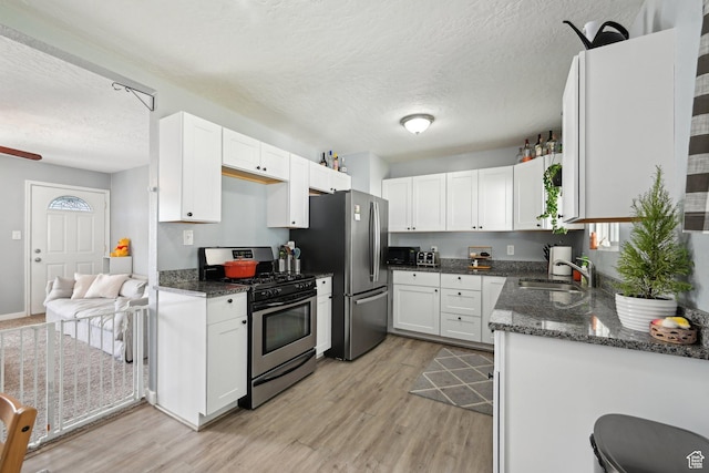 293 E Valley View Dr, Tooele, UT 84074 - kitchen featuring a textured ceiling, light wood-style flooring, dark stone countertops, stainless steel appliances, and white cabinetry