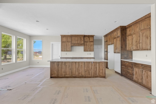 2881 N 3475 W Unit 17, Plain City, UT 84404 - kitchen with light countertops, a textured ceiling, brown cabinetry, a center island, and baseboards