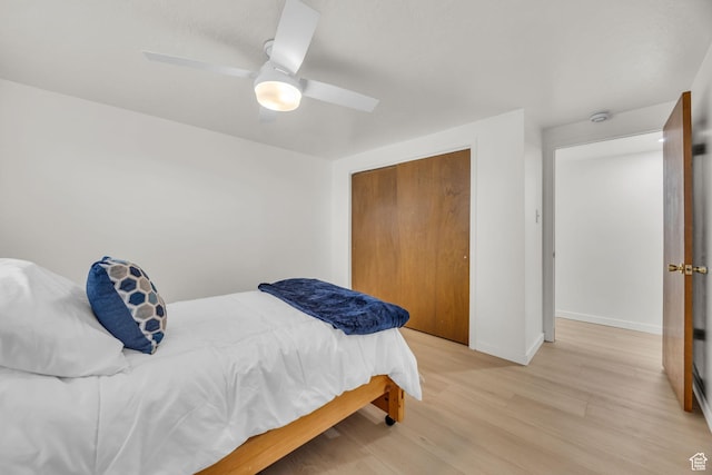 bedroom featuring baseboards, ceiling fan, light wood-style flooring, and a closet
