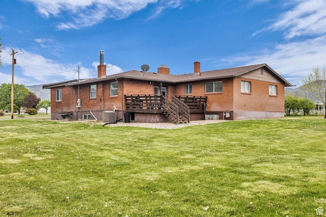 rear view of property featuring brick siding, a wooden deck, a yard, and a chimney