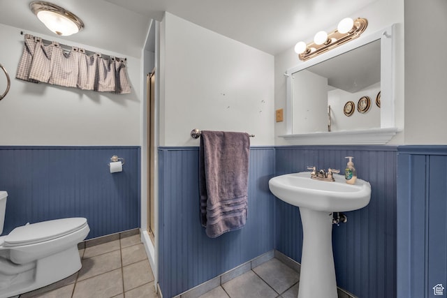 full bath with a wainscoted wall, tile patterned floors, a shower with shower door, and toilet