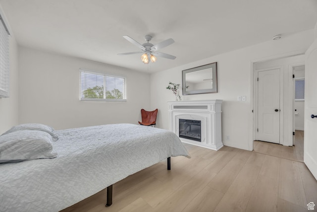 bedroom with baseboards, a ceiling fan, light wood-style flooring, and a glass covered fireplace