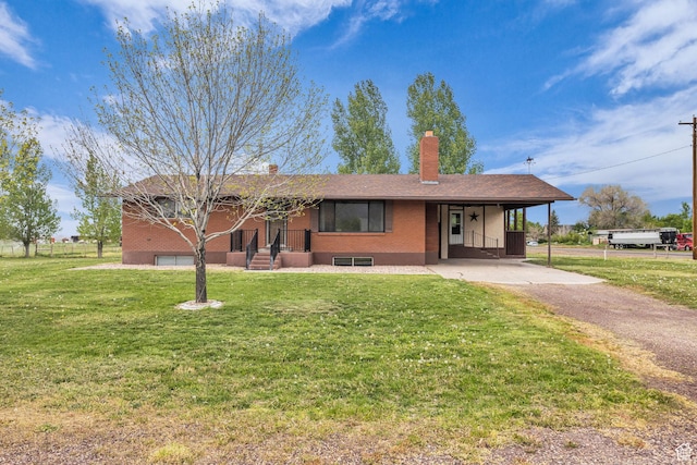 ranch-style home featuring brick siding, an attached carport, a front yard, a chimney, and driveway