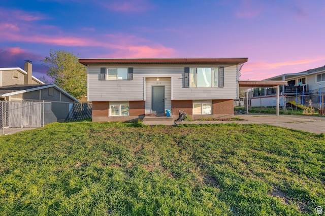 split foyer home with a lawn, brick siding, fence, and a carport
