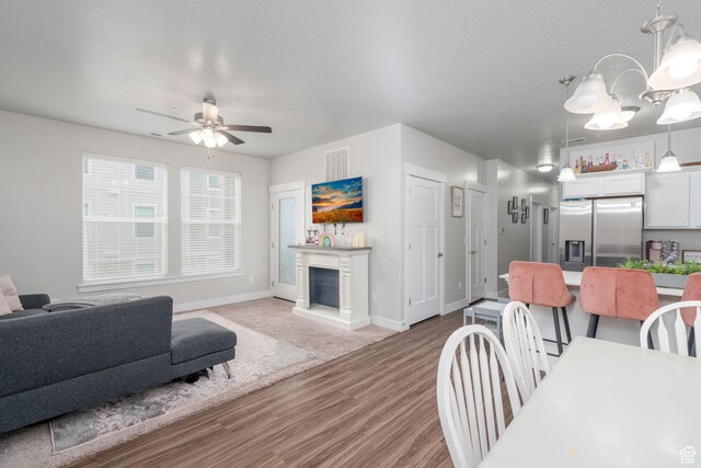 1809 W Terra Vista Ln Unit H101, Saratoga Springs, UT 84045 - living room with a fireplace, ceiling fan with notable chandelier, baseboards, wood finished floors, and visible vents