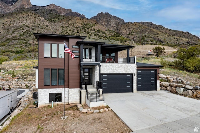contemporary house featuring a mountain view, stone siding, concrete driveway, and a balcony