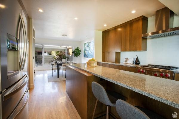 2812 E Commonwealth Ave S, Salt Lake City, UT 84109 - kitchen featuring stainless steel fridge, light wood-style floors, brown cabinetry, wall chimney exhaust hood, and modern cabinets