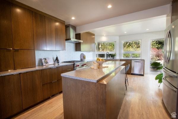 2812 E Commonwealth Ave S, Salt Lake City, UT 84109 - kitchen with appliances with stainless steel finishes, light wood finished floors, wall chimney exhaust hood, a kitchen island, and modern cabinets