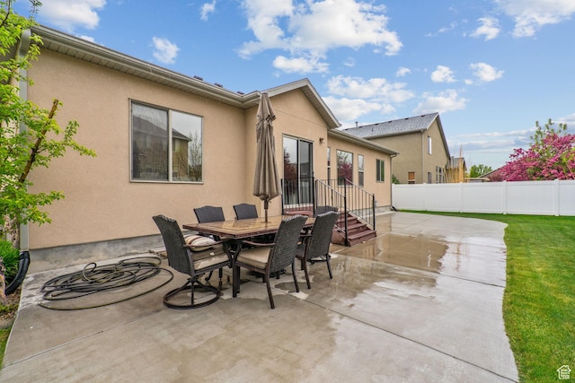 rear view of house featuring fence, a patio, stucco siding, and outdoor dining space