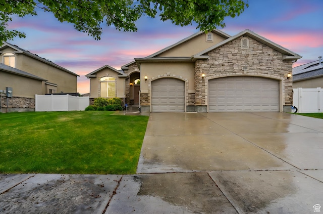 view of front facade with driveway, fence, a yard, an attached garage, and stone siding